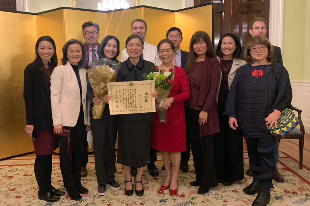 Shoko Hamano smiling and holding a certificate with several other people standing around her smiling